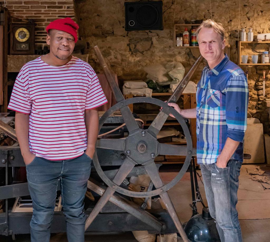 Mongezi Ncaphayi et Francis van der Riet, se tiennent debout près de la presse dans l'atelier le grand Village